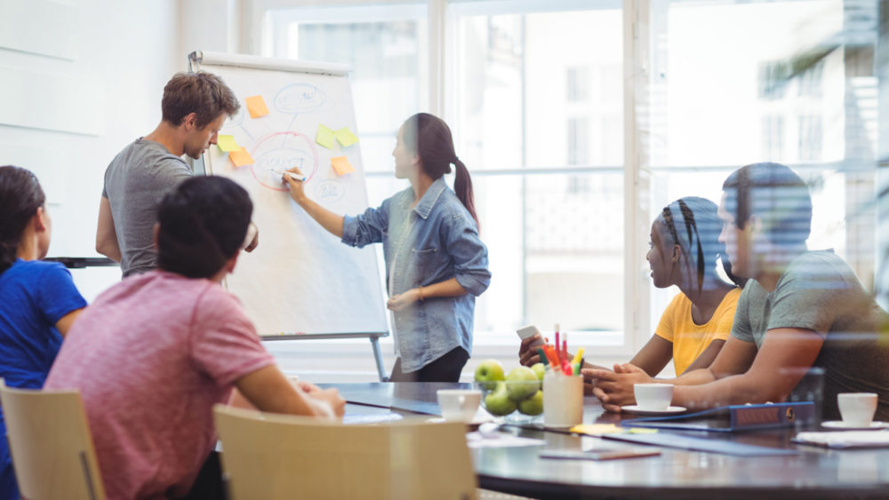 Business executives discussing with their colleagues on whiteboard during meeting at office