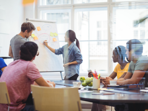 Business executives discussing with their colleagues on whiteboard during meeting at office